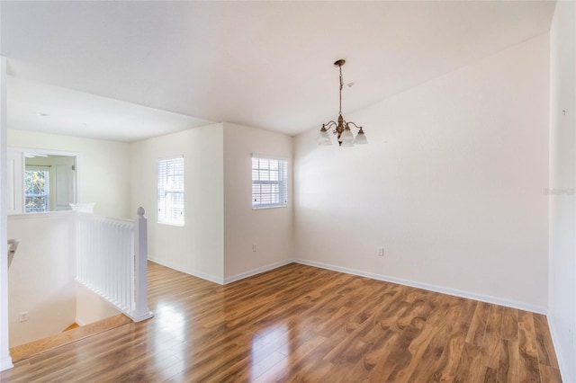 unfurnished room with a notable chandelier, baseboards, and wood finished floors