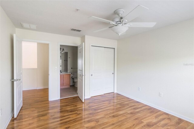 unfurnished bedroom featuring a closet, visible vents, light wood-style flooring, a ceiling fan, and ensuite bath