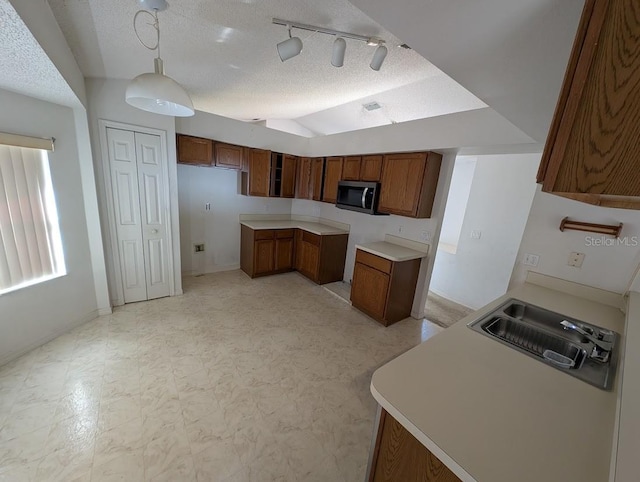 kitchen featuring lofted ceiling, a textured ceiling, a sink, brown cabinetry, and stainless steel microwave