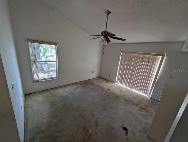 carpeted empty room featuring ceiling fan, vaulted ceiling, and a textured ceiling