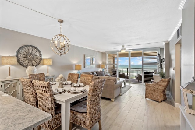 dining space featuring visible vents, a water view, crown molding, ceiling fan with notable chandelier, and light wood-type flooring