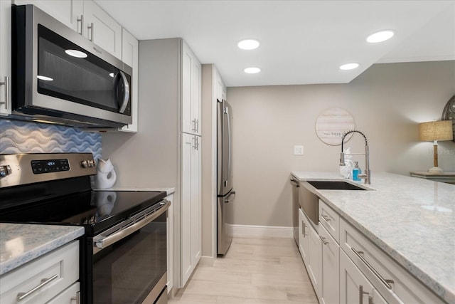 kitchen with light stone counters, recessed lighting, a sink, stainless steel appliances, and white cabinetry