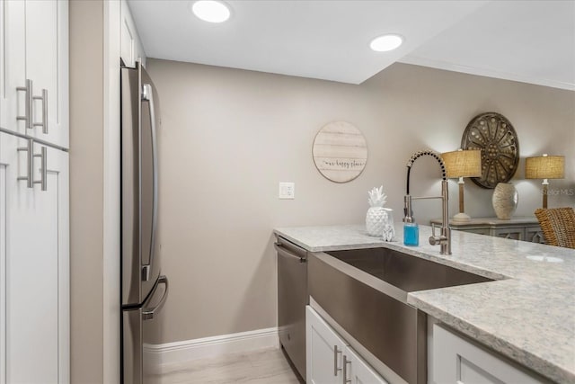 kitchen with a sink, light stone counters, white cabinetry, appliances with stainless steel finishes, and baseboards