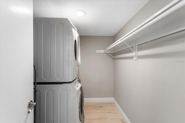 clothes washing area with stacked washer / dryer, light wood-style flooring, laundry area, and baseboards