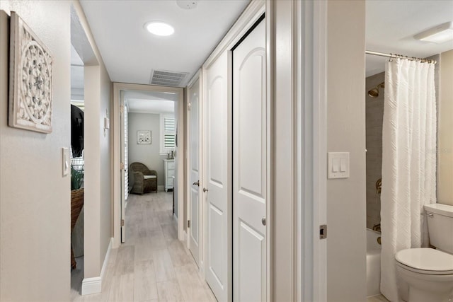 hall with visible vents, baseboards, and light wood-style floors