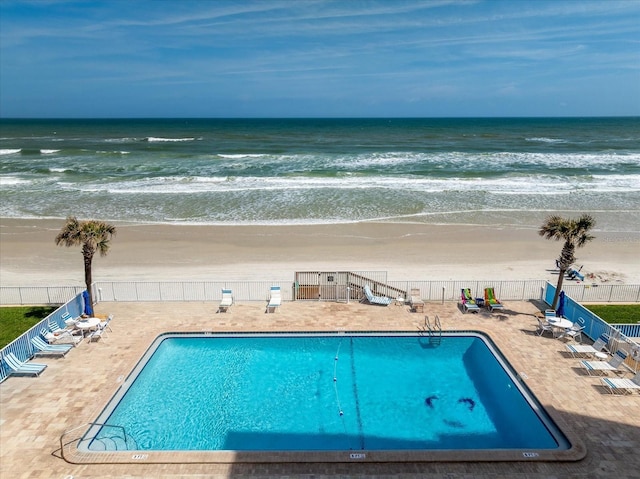 pool featuring a patio area, a beach view, fence, and a water view