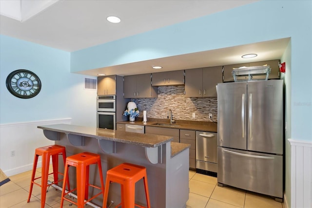 kitchen featuring light tile patterned floors, a sink, stainless steel appliances, a kitchen breakfast bar, and tasteful backsplash