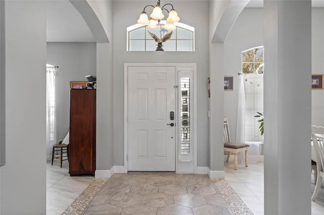 foyer entrance with a towering ceiling, an inviting chandelier, baseboards, and arched walkways