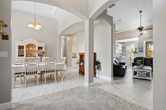 dining area with visible vents, baseboards, a towering ceiling, marble finish floor, and ceiling fan with notable chandelier