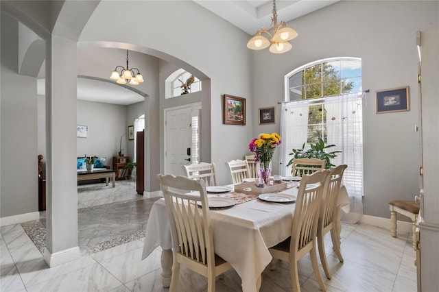 dining space featuring a chandelier, marble finish floor, arched walkways, and baseboards