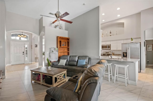 living room with arched walkways, baseboards, a towering ceiling, ceiling fan, and recessed lighting