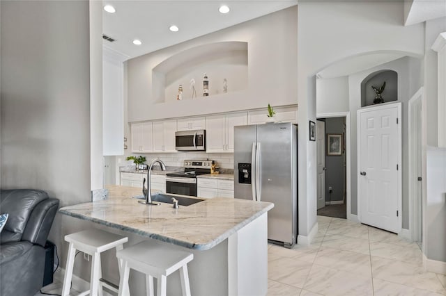 kitchen featuring marble finish floor, a high ceiling, appliances with stainless steel finishes, white cabinetry, and a sink