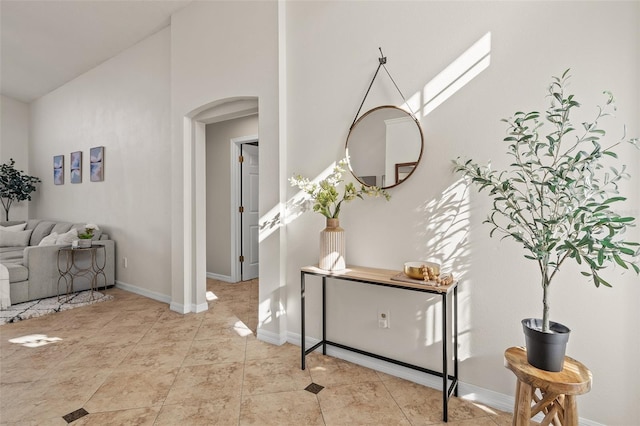 corridor with arched walkways, tile patterned floors, and baseboards