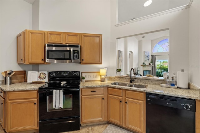 kitchen featuring a sink, light stone countertops, black appliances, and a towering ceiling