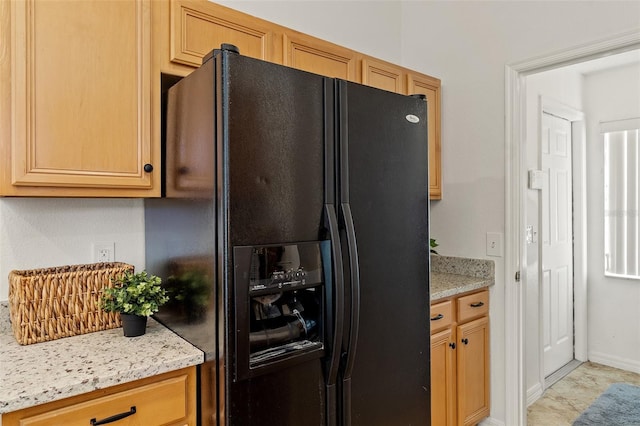 kitchen with light stone counters, black fridge with ice dispenser, and baseboards