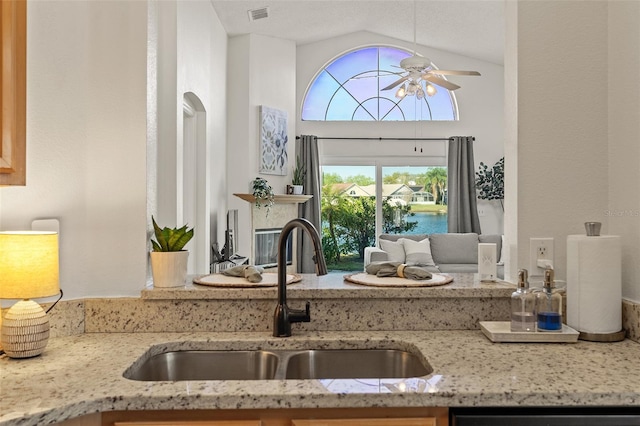 kitchen featuring light stone counters, a ceiling fan, visible vents, high vaulted ceiling, and a sink