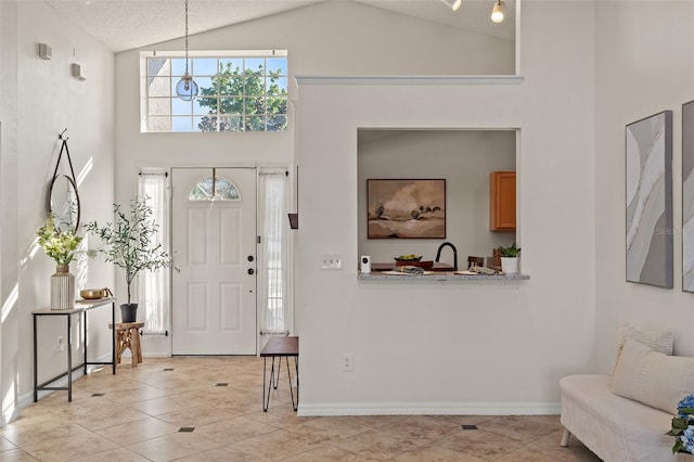 foyer featuring light tile patterned floors, a textured ceiling, high vaulted ceiling, and baseboards