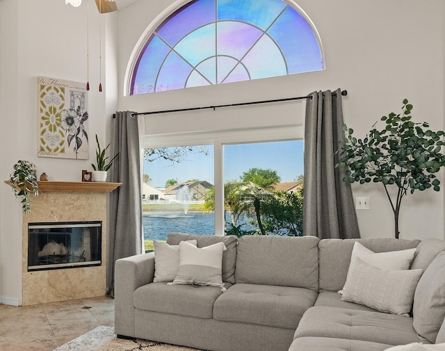 tiled living area featuring ceiling fan, a fireplace, and a towering ceiling