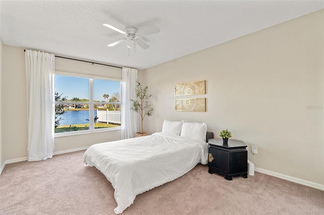 bedroom with baseboards, carpet, a ceiling fan, and a water view