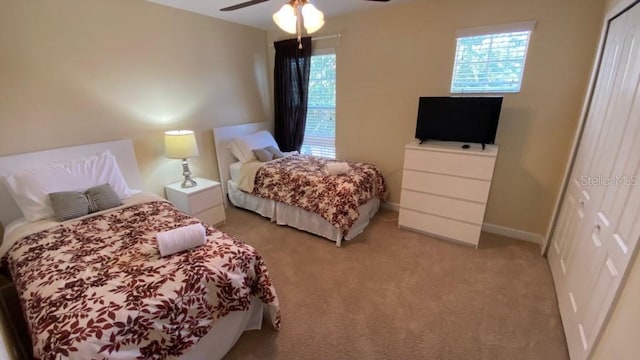 bedroom featuring a closet, baseboards, light colored carpet, and a ceiling fan