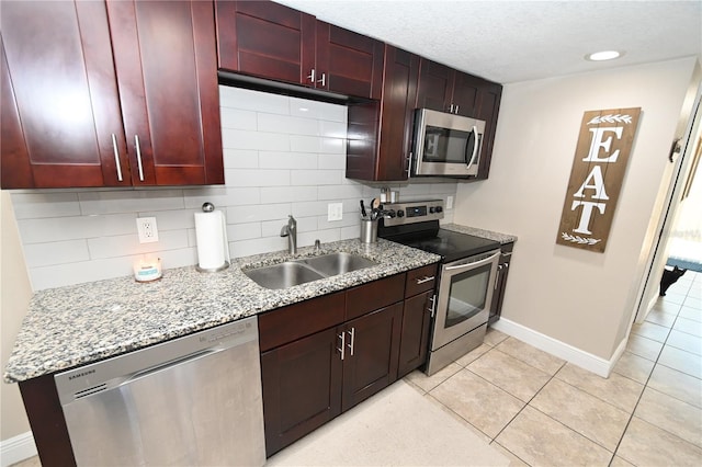 kitchen featuring a sink, appliances with stainless steel finishes, decorative backsplash, light stone countertops, and dark brown cabinets