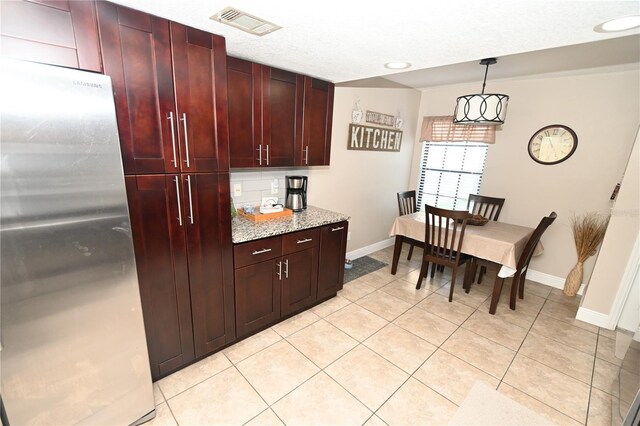 kitchen with visible vents, freestanding refrigerator, light tile patterned flooring, dark brown cabinets, and hanging light fixtures