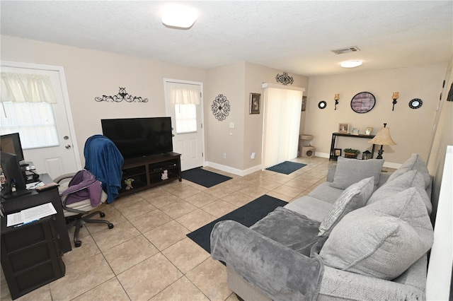 living area featuring light tile patterned floors, visible vents, a textured ceiling, and baseboards