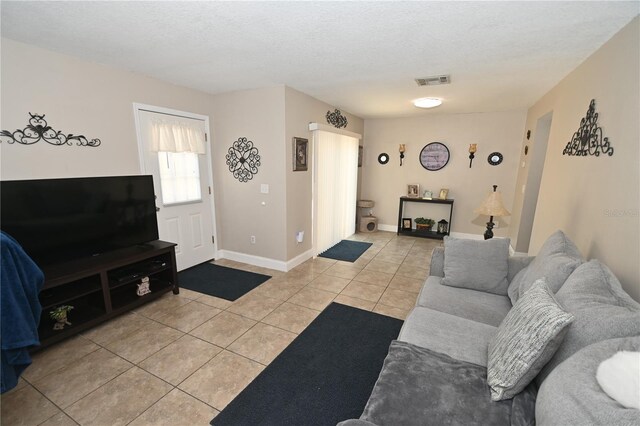 living room with light tile patterned floors, baseboards, visible vents, and a textured ceiling