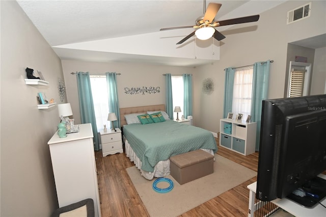 bedroom with lofted ceiling, multiple windows, wood finished floors, and visible vents