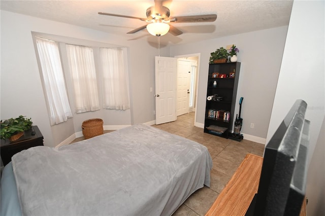 bedroom with baseboards, a textured ceiling, light tile patterned flooring, and a ceiling fan