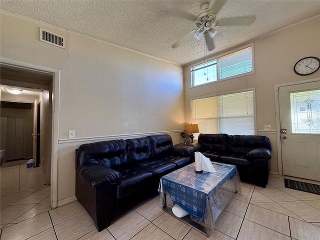 living room featuring light tile patterned floors, visible vents, a textured wall, ceiling fan, and a textured ceiling