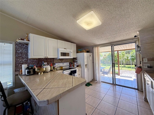 kitchen with lofted ceiling, light tile patterned floors, a peninsula, white appliances, and white cabinets