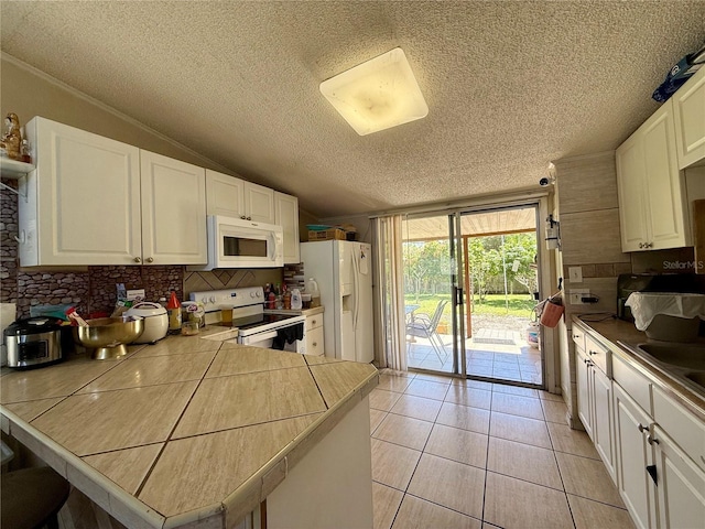 kitchen featuring light tile patterned floors, lofted ceiling, white appliances, white cabinets, and tasteful backsplash