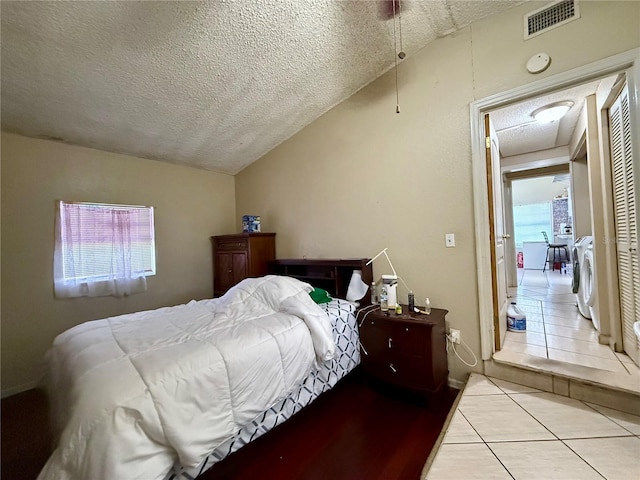 bedroom featuring washer and clothes dryer, visible vents, vaulted ceiling, a textured ceiling, and tile patterned floors