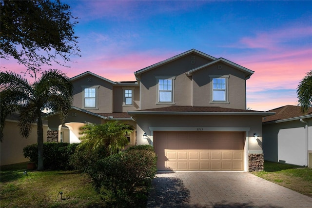 traditional-style house with stone siding, stucco siding, decorative driveway, and an attached garage