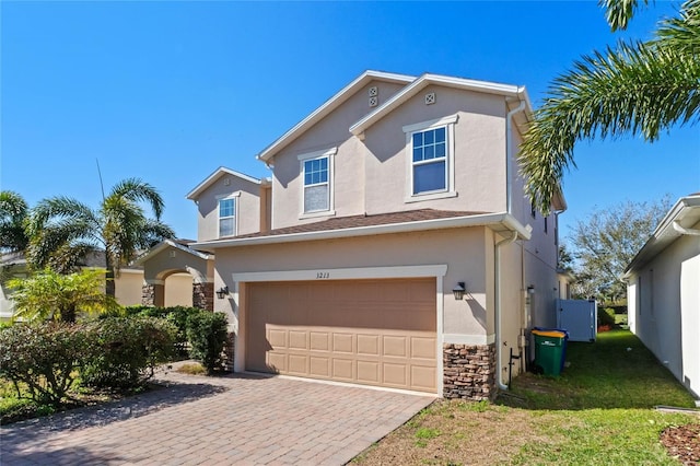 traditional-style home with stucco siding, stone siding, a garage, and decorative driveway