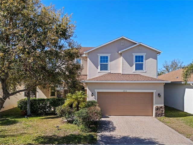 traditional-style house with stucco siding, decorative driveway, an attached garage, a shingled roof, and a front yard