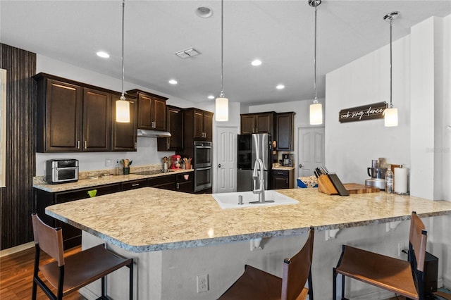 kitchen with visible vents, a sink, dark brown cabinetry, appliances with stainless steel finishes, and a kitchen bar