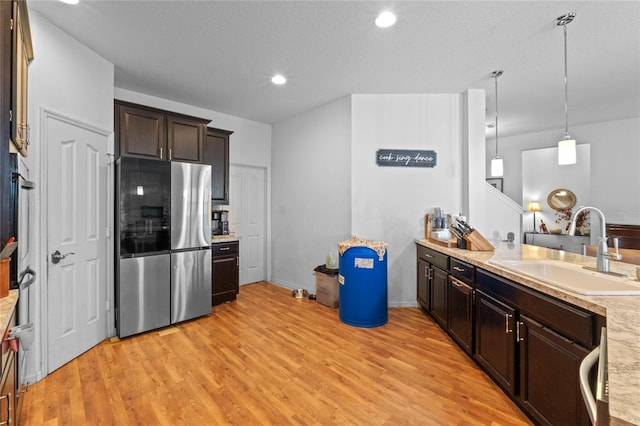 kitchen featuring light wood-style flooring, freestanding refrigerator, a sink, light countertops, and dark brown cabinets