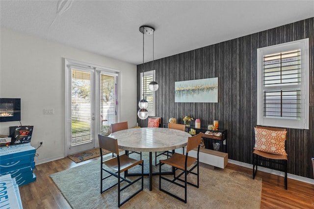 dining room with wallpapered walls, an accent wall, baseboards, and wood finished floors