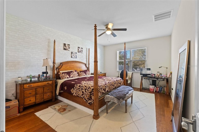 bedroom featuring visible vents, a ceiling fan, wood finished floors, and brick wall