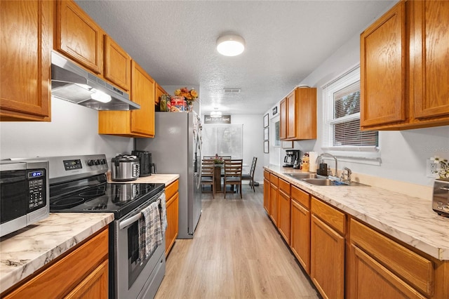 kitchen with appliances with stainless steel finishes, light countertops, light wood-type flooring, under cabinet range hood, and a sink