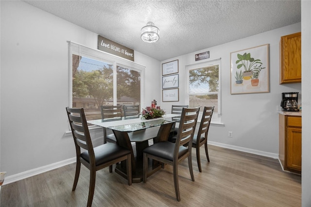 dining space featuring light wood-style floors, a textured ceiling, and baseboards