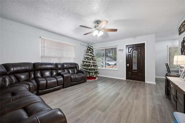 living room with ceiling fan, a textured ceiling, baseboards, and wood finished floors