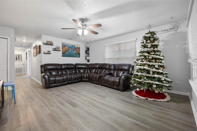 living room featuring baseboards, visible vents, a ceiling fan, wood finished floors, and a textured ceiling