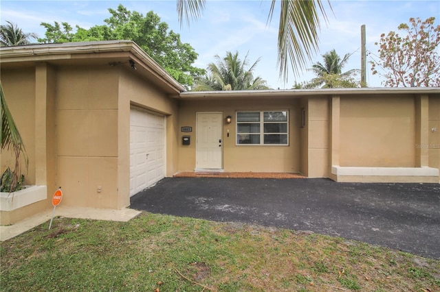 property entrance with an attached garage, aphalt driveway, and stucco siding