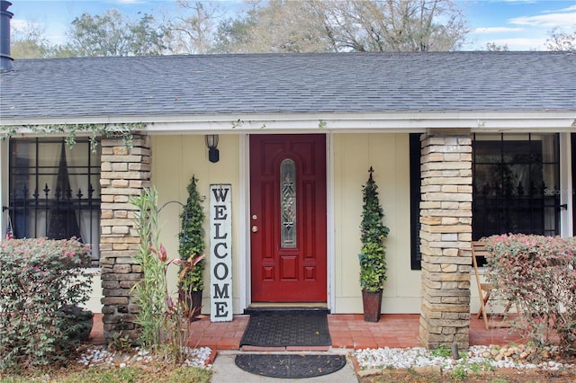 view of exterior entry with stone siding, roof with shingles, and brick siding