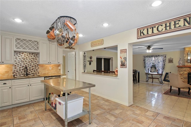 kitchen with a textured ceiling, a fireplace, a sink, stainless steel dishwasher, and decorative backsplash