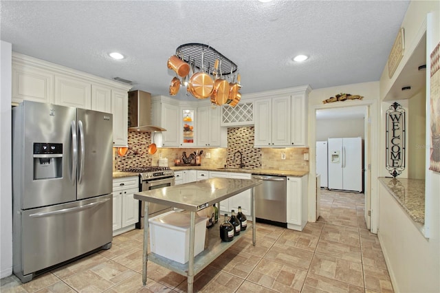 kitchen featuring tasteful backsplash, wall chimney exhaust hood, stainless steel appliances, and a sink