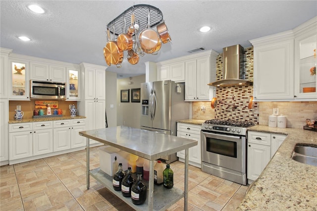 kitchen featuring recessed lighting, white cabinets, wall chimney range hood, appliances with stainless steel finishes, and tasteful backsplash